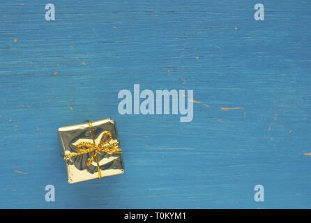 Goldene Geschenk Box auf einem blauen Hintergrund aus Holz mit Platz für Text Stockfoto