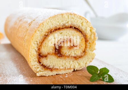 Lecker keks Rolle mit Aprikosenmarmelade auf einem weißen Holztisch. Schneiden close-up. Dessert für Frühstück. Stockfoto