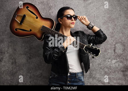 Weibliche Gitarristen stützte sich auf eine rostige graue Wand Stockfoto