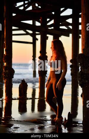 Attraktive junge Frau im Yoga Hosen unter Crystal Pier stehend beobachten Sonnenuntergang bei der Tide langsam kommt, Pacific Beach, San Diego, CA, USA Stockfoto