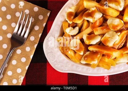 Poutine Platte auf einer rot-schwarz karierte Tischdecke. Mahlzeit mit Pommes frites, Rindfleisch, Soße und Quark Käse gekocht. Kanadische Küche. Stockfoto