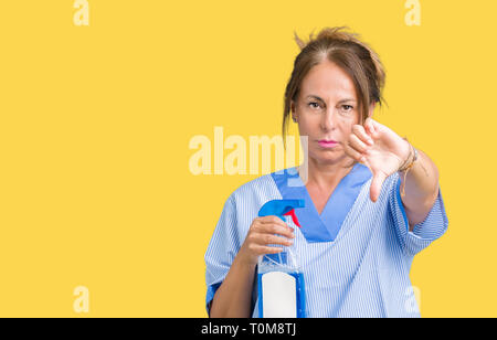 Mittleres Alter brunette Reiniger Frau tragen die Hausarbeit gleichmäßig über isolierte Hintergrund mit Verärgerten Gesicht, negatives Vorzeichen zeigen Abneigung mit Daumen nach unten, Stockfoto