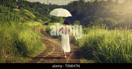 Ein Mädchen in einem weißen Kleid auf dem Weg des Künstlers. Mädchen mit einem Regenschirm. Bali Reise. Tropen. Campuhan Ridge zu Fuß reisen. Stockfoto