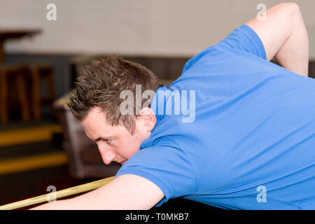 Männlicher Poolspieler mit geliertem Stachelhaar, er ist in einer Bar und spielt Billard. Er beugt sich über den Tisch, um den Topf zu versenken. Stockfoto