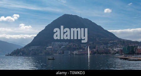 Der Brunnen in den See und ein Fischerboot, Blick auf den See von Lugano und den Monte San Salvatore, Schweiz Stockfoto