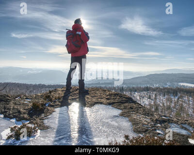 Stehende Mann mit angehobenem Arm auf eisigen Stein und Blick auf schneebedeckte Berge. Landschaft mit Reisende, Stockfoto