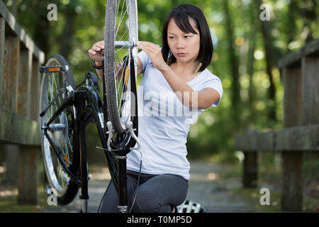 Junge Frau, die versucht, ihr Fahrrad im Park zu beheben Stockfoto