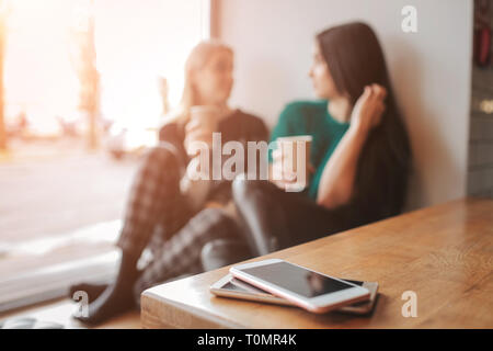 Zwei junge Frau in einem Café zu plaudern. Zwei Freunde Kaffee zusammen genießen. Ihre Smartphones in Haufen liegen auf der Tabelle auf der Vordergrund. Stockfoto