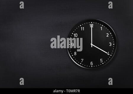 Wanduhr mit vier Uhr auf schwarzem Hintergrund auf dem Schwarzen Brett. Büro Uhr zeigt 4 Uhr oder 4 Uhr an schwarze Textur Stockfoto