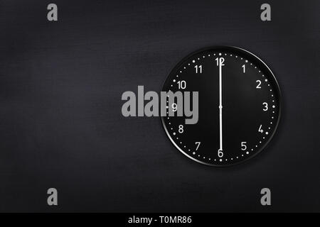 Wanduhr mit sechs Uhr auf schwarzem Hintergrund auf dem Schwarzen Brett. Büro Uhr zeigt 6:00 oder 6:00 Uhr am Schwarzen Textur Stockfoto
