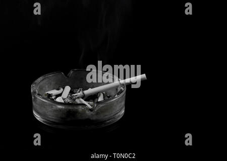 Zigarette geraucht auf volle Aschenbecher auf schwarzem Hintergrund Stockfoto