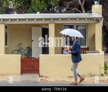 Kaukasische Mann mit einem weißen Sonnenschirm und trägt blaue Jacke vorbei gehen. Ein Ferienhaus auf Rottnest Island WA Australien. Stockfoto