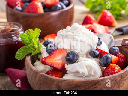Nahaufnahme der eine hölzerne Schüssel mit Vanilleeis mit Blaubeeren und Erdbeeren Stockfoto
