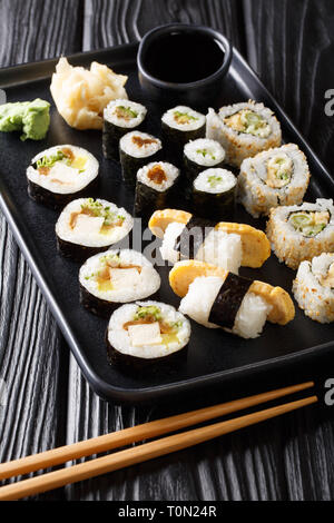 Die japanischen Hosomaki rollt, Uramaki, Maki, Nigiri, Tamagoyaki mit verschiedenen Füllungen close-up auf einem Teller auf den Tisch. Vertikale Stockfoto