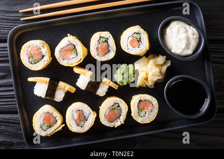 Sushi Roll im Omelette mit Reis, Käse, Lachs und Avocado closeup mit Soßen, Wasabi und Ingwer auf einem Teller auf den Tisch serviert. Horizontal oben Stockfoto