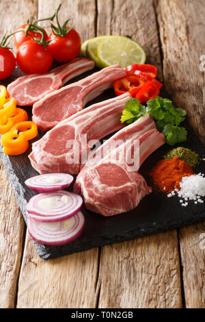 Raw Lammkoteletts mit frischem Gemüse und Gewürze close-up auf einer Schiefertafel Board auf dem Tisch. Vertikale Stockfoto