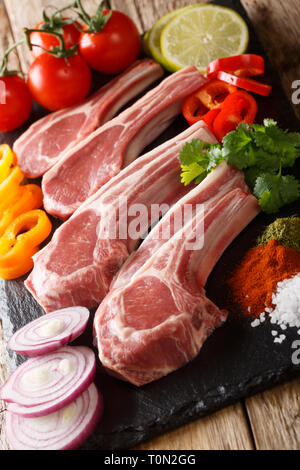 Frisches rohes Lammkotelett mit Knochen mit pflanzlichen Zutaten close-up auf den Tisch. Vertikale Stockfoto