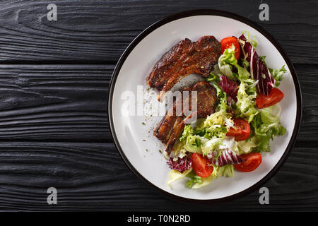 Lecker gebratenen Lammkoteletts mit frischen Salat in der Nähe serviert auf einem Teller auf den Tisch. Horizontal oben Ansicht von oben Stockfoto