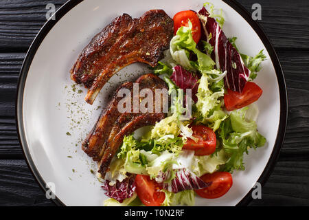 Gebackene Lamm Steak mit Honig mit frischem Salat in der Nähe serviert auf einem Teller auf den Tisch. Horizontal oben Ansicht von oben Stockfoto