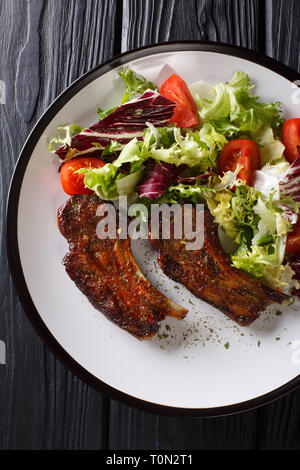 Gebackene Lamm Steak mit Honig mit frischem Salat in der Nähe serviert auf einem Teller auf den Tisch. Vertikal oben Ansicht von oben Stockfoto