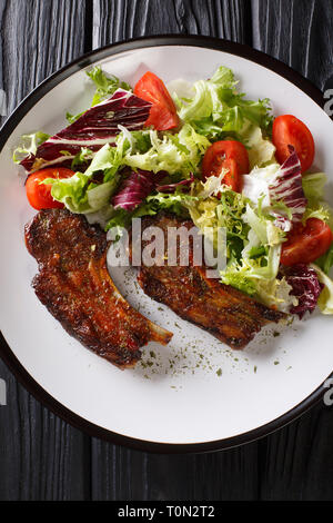 Lecker gebratenen Lammkoteletts mit frischen Salat in der Nähe serviert auf einem Teller auf den Tisch. Vertikal oben Ansicht von oben Stockfoto