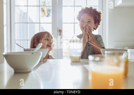 Zwei Kinder am Frühstückstisch mit Flasche Milch und Saft am Tisch sitzen. Fröhliche Kinder, die Spaß und lächelnd auf dem Frühstückstisch. Stockfoto