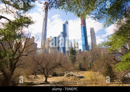 Wolkenkratzer von Manhattan gesehen durch eine Pause im Laub im Central Park, New York City, New York. Essex Haus, 2020 Central Park Süd & andere Stockfoto
