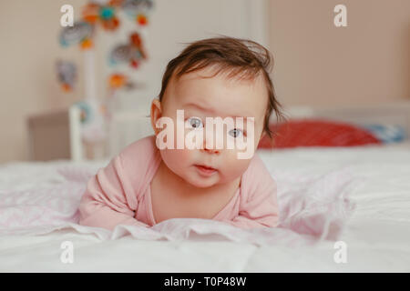 Portrait von cute adorable Asiatischen gemischten Rennen Baby Mädchen vier Monate alten liegend auf Bauch auf dem Bett im Schlafzimmer in Kamera schaut. Natürliches Gefühl Gesicht expressi Stockfoto