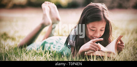 Lächelndes Mädchen auf dem Rasen liegen und Buch im park Stockfoto