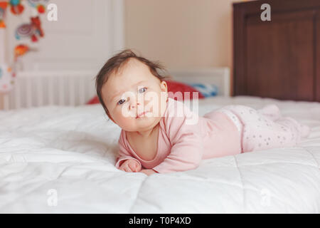 Portrait von cute adorable Asiatischen gemischten Rennen Baby Mädchen vier Monate alten liegend auf Bauch auf dem Bett im Schlafzimmer in Kamera schaut. Natürliches Gefühl Gesicht expressi Stockfoto