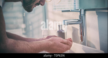 Mann sein Gesicht mit Wasser im Bad waschen Stockfoto