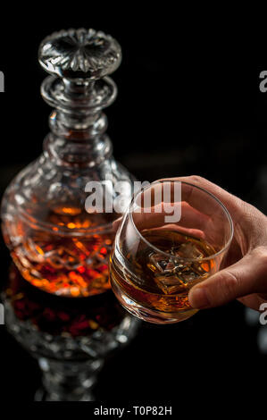 Whiskey Glas halten von Menschen Hand und Kristall Karaffe auf dunklem Hintergrund. Selektive konzentrieren. Kopieren Sie Platz. Stockfoto
