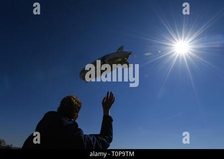 Friedrichshafen, Deutschland. 21 Mär, 2019. Der Zeppelin NT (Neue Technologie) nimmt neben dem Zeppelin Hangar am Anfang der Saison, während ein Zuschauer Wellen, die die Gäste in der Gondel. Credit: Felix Kästle/dpa/Alamy leben Nachrichten Stockfoto