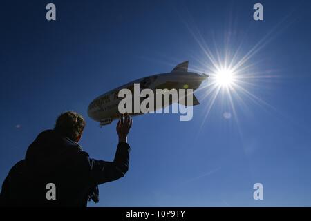 Friedrichshafen, Deutschland. 21 Mär, 2019. Der Zeppelin NT (Neue Technologie) nimmt neben dem Zeppelin Hangar am Anfang der Saison, während ein Zuschauer Wellen, die die Gäste in der Gondel. Credit: Felix Kästle/dpa/Alamy leben Nachrichten Stockfoto