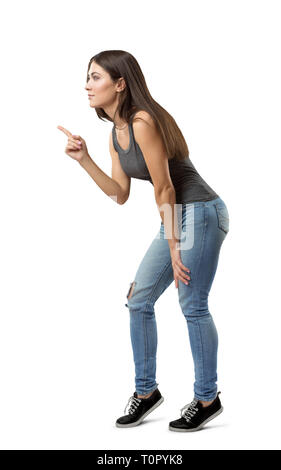 Seitenansicht der jungen schönen Frau in Grau Top und Jeans nach vorne beugen, der auf etwas mit Zeigefinger auf weißem Hintergrund. Stockfoto