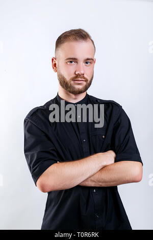 Porträt der jungen gutaussehenden Mann im schwarzen T-Shirt stand mit verschränkten Armen auf grauem Hintergrund Stockfoto