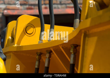 Hydraulikschläuche Verbindungen und andere Mechanismen der gelben Maschinen close-up auf einem unscharfen Hintergrund der alten Mauer Stockfoto