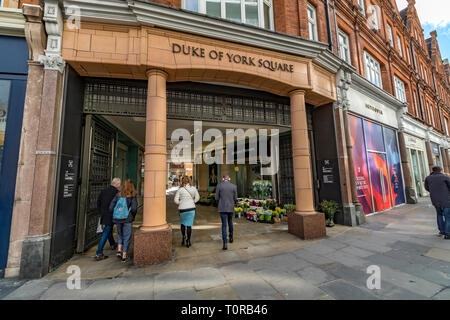 Menschen, die durch den Eingang zum Duke of York Square, Sloane Square, Chelsea, London, Großbritannien gehen Stockfoto