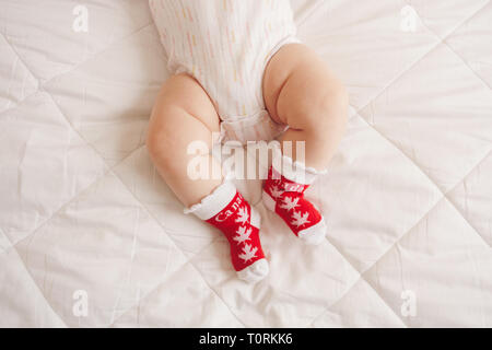 Nahaufnahme des Weißen chubby Baby Beine Füße das Tragen der roten Socken mit kanadische Maple Leaf Flag. Kind Kind liegend auf Bett in Kleidung mit nationalen Symbol von C Stockfoto