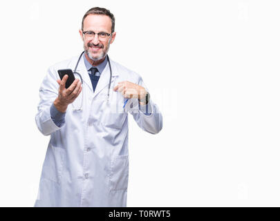Mittleres Alter senior hoary Arzt Mann texting mit Smartphone über isolierte Hintergrund mit Überraschung Gesicht zeigenden Finger zu sich selbst Stockfoto