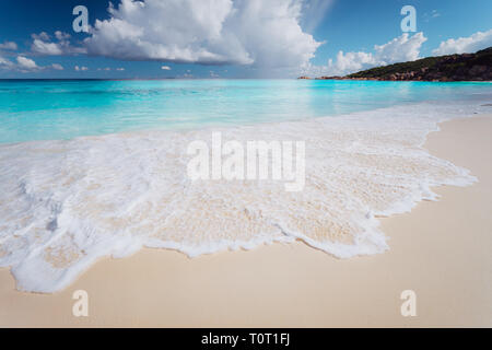 Super Wasser Farben von Grande Anse, La Digue Island Seychellen. Sea Foam am tropischen Strand mit weißen Wolken. Ferienhäuser Hintergrund Stockfoto