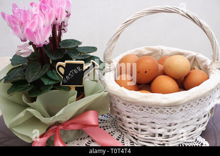 Ostern Dekoration mit weißen Weidenkorb voll von natürlichen organischen frischen Hühnereiern und rosa Cyclamen mit pinky Schleifchen verziert Stockfoto