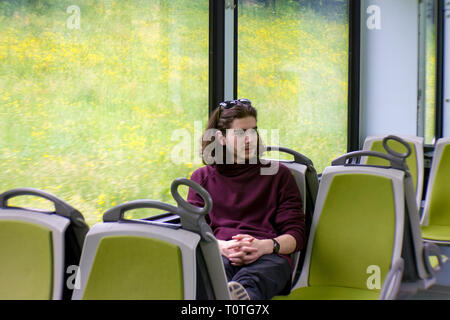 Ein hübscher Kerl fährt eine S-Bahn, sitzt und schaut aus dem Fenster, draußen vor dem Fenster ist eine blühende Frühlingswiese. Stockfoto