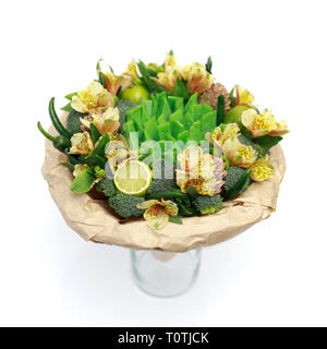 Originelles Geschenk in Form von einem Strauß Blumen, Gemüse und grünem Käse, stehend in einem Glas Vase auf einem weissem Hintergrund Stockfoto