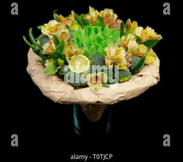 Originelles Geschenk in Form von einem Strauß Blumen, Gemüse und grünem Käse, stehend in einem Glas Vase auf einem schwarzen Hintergrund isoliert Stockfoto