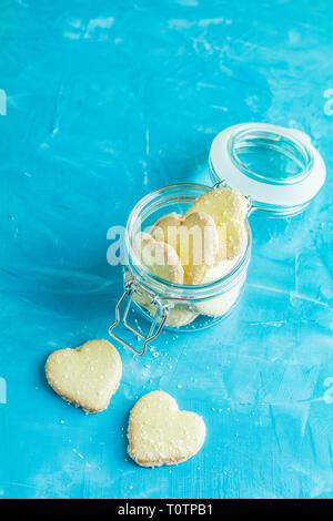 Köstliche gebackene Kekse in Herzform mit Kokos Chips in Glas Glas auf blauen Beton Tabelle Oberfläche. Essen Grußkarte mit kopieren Sie Text. Stockfoto