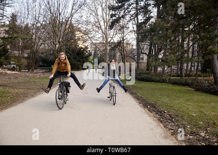 Zwei Jugendliche, 20-29 Jahre alt, mit dem Fahrrad in einem Park mit Beine gestreckt, dumm, lachen und Spaß haben. Stockfoto