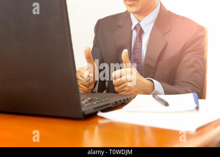 Geschäftsmann mit Daumen hoch, am Arbeitsplatz mit Laptop auf dem Schreibtisch. Stockfoto