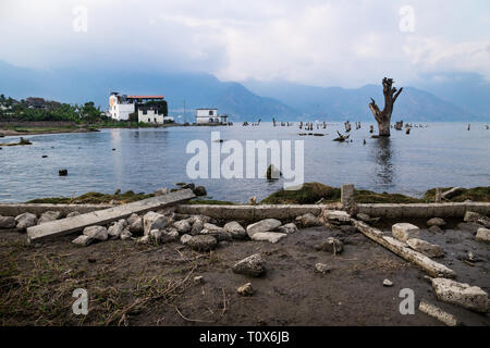 Küste Blick auf Lake Atitlan mit toten Baum, Haus und mountainrange, San Pedro de la Laguna, Guatemala Stockfoto