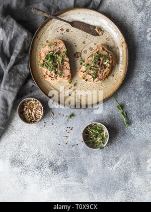 Zwei Toast Ente mit Backpflaumen rillettes Pastete auf Weißbrot mit Sprossen und verschiedenen Samen auf eine alte Platte auf grauem Hintergrund. Stockfoto